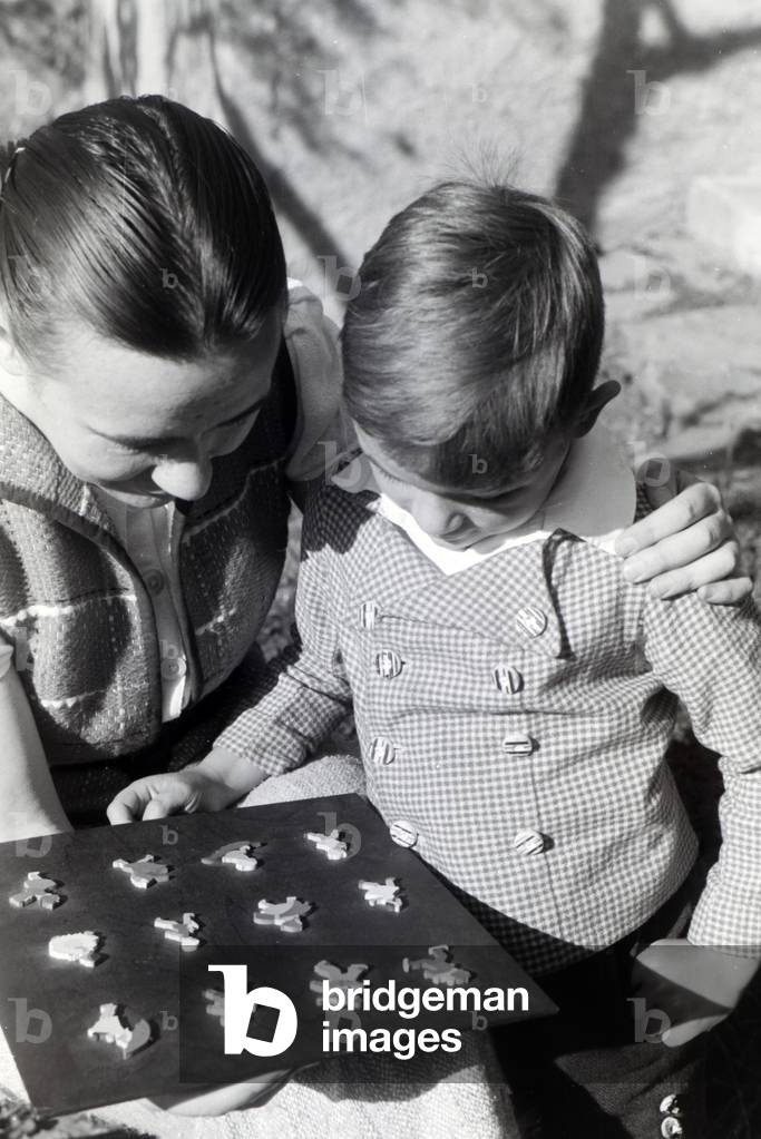 Magda Heller, who founded the company Heller Kunst in the Eifel together with her husband Georg, showing little wooden figures to her son, Germany 1930s (b/w photo)