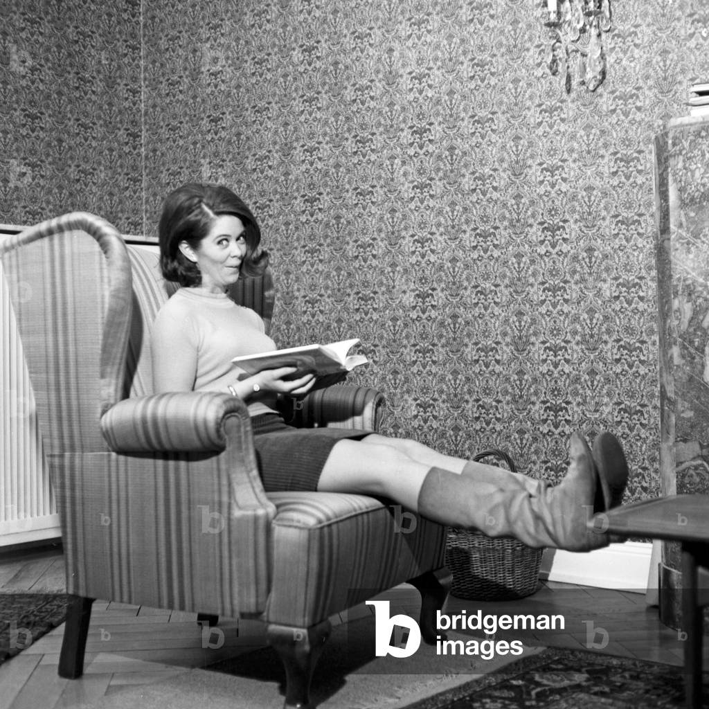 Norwegian schlager singer Wencke Myhre having fun with a book in the chair of the living room, 1960s