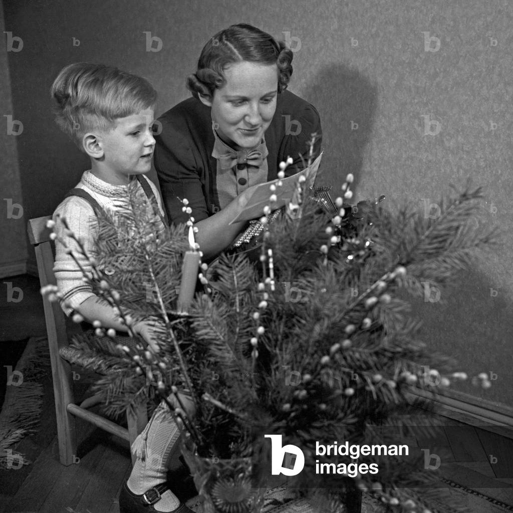 A little boy typing his list of wishes and gives it his mother for forwarding to Santa, Germany 1930s (b/w photo)