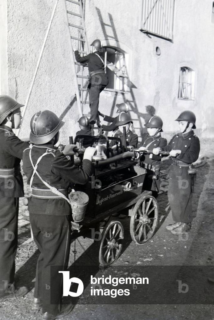 A group of junior firefighters is preparing the firewagon and ladder during a firefighter training, Germany 1930s (b/w photo)