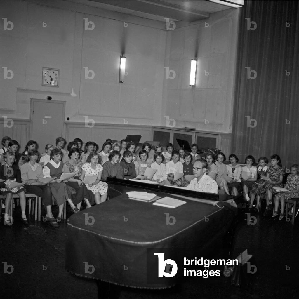 Composer and leader of the NDR children's choir, Erich Bender, composing on his grand piano with the choir, Germany 1950s