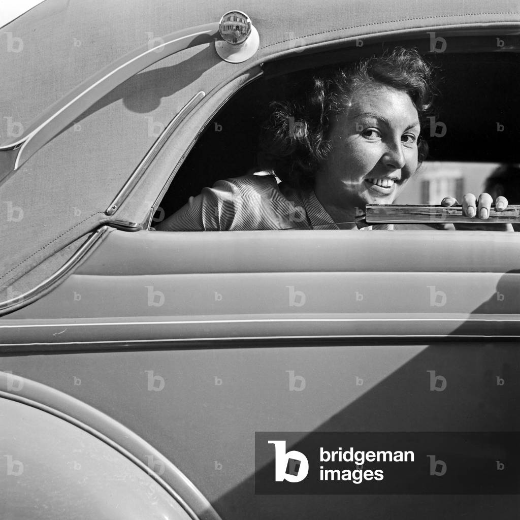 A young female looking out of the window of a closed convertible Ford V8, Germany 1930s (b/w photo)