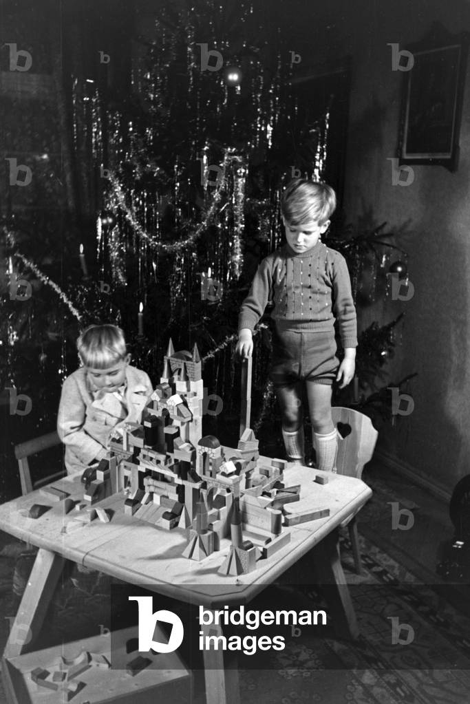Two boys playing with the new set of toy blocks under the christmas tree, Germany 1930s (b/w photo)