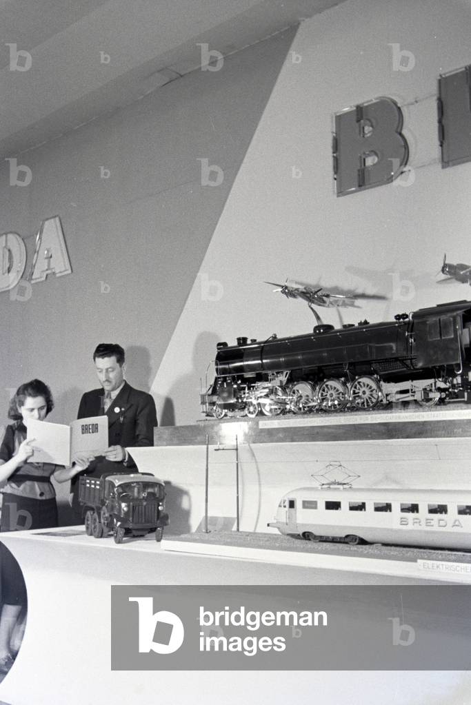 Two Persons in front of a stand with models of the italian mechanical engineering corporation Breda on the Leipziger Frühjahrsmesse, Germany 1941 (b/w photo)