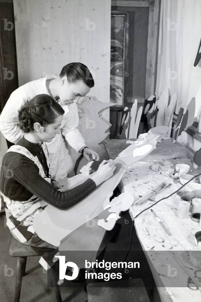 Magda Heller and an employee of the Heller Kunst workshops in the Eifel who is painting a sawn out wooden figure, Germany 1930s (b/w photo)