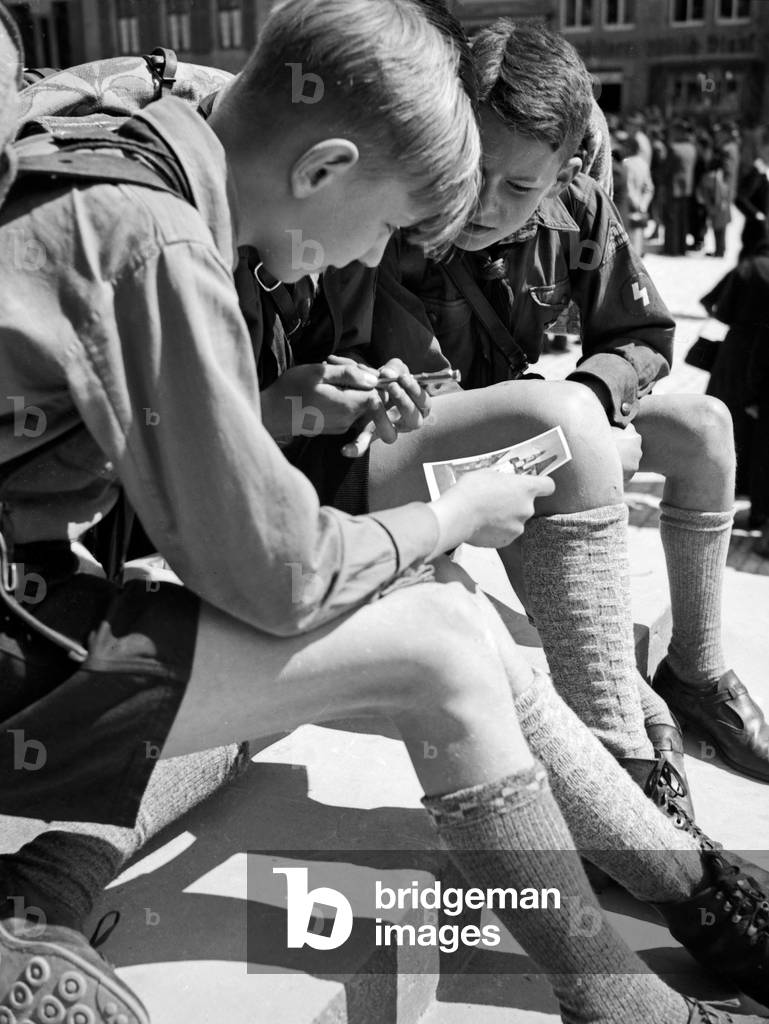 Three Hitler youths writing a postcard from a wandering trip, Germany 1930s (b/w photo)