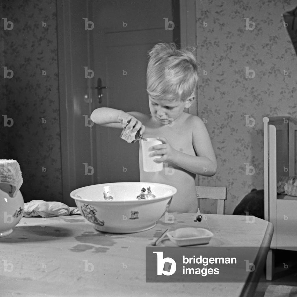 A little boy taking a sip of mouthwash for gargling, Germany 1930s (b/w photo)