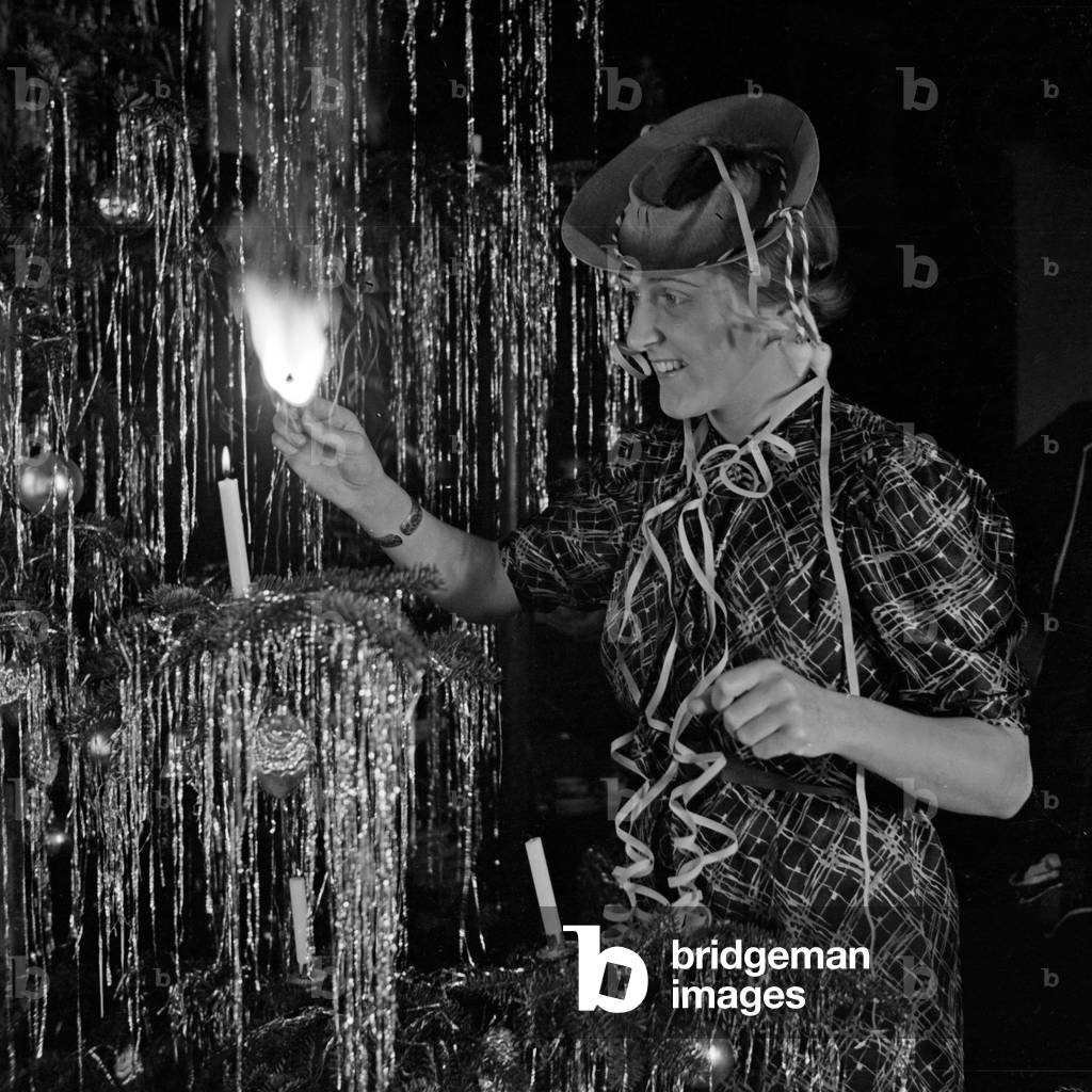 A young woman lighting the candles at the christmas tree on new year's eve, Germany 1930s (b/w photo)