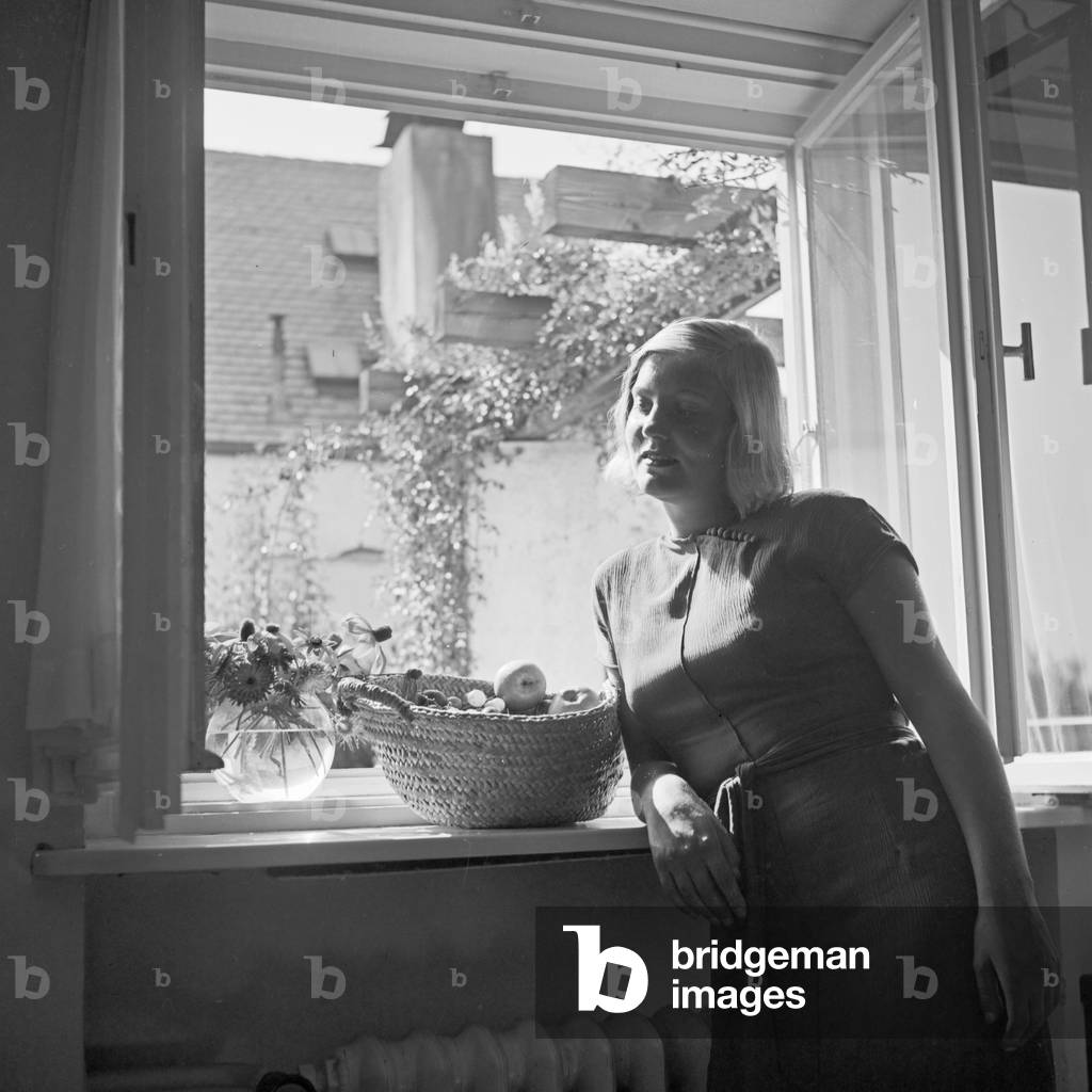 A young woman at the window with a basket of fruits, Germany 1930s (b/w photo)
