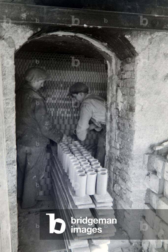 Employees of a stoneware factory are stacking ceramic blanks inside a drying room, Germany 1930s (b/w photo)