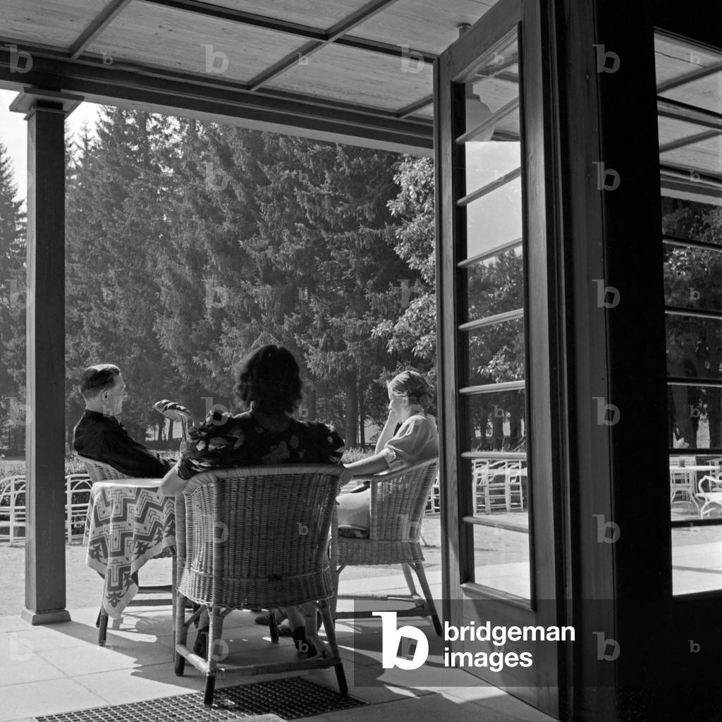 A man and two women sitting in the patio of the spa resort at Herrenalb in Black Forest, Germany 1930s (b/w photo)