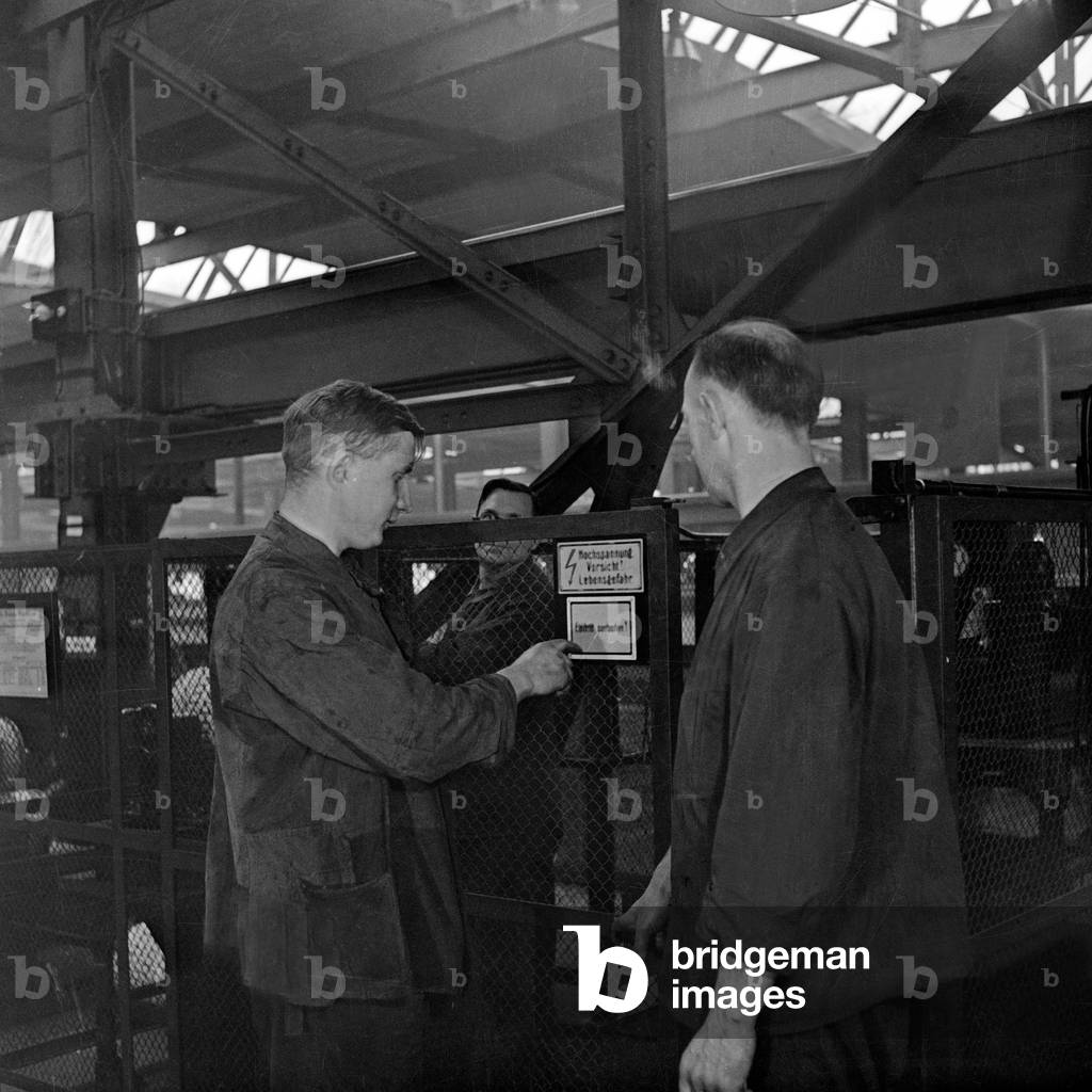 Worker and warning signs of high voltage at a railway reparing factory, Germany 1930s (b/w photo)