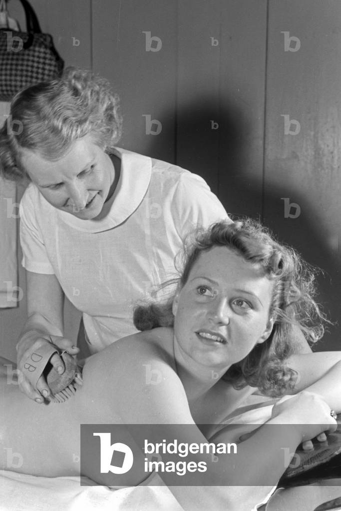 A young woman gets a massage with a brush at Admiralsbad bath in Berlin, Germany 1930s (b/w photo)