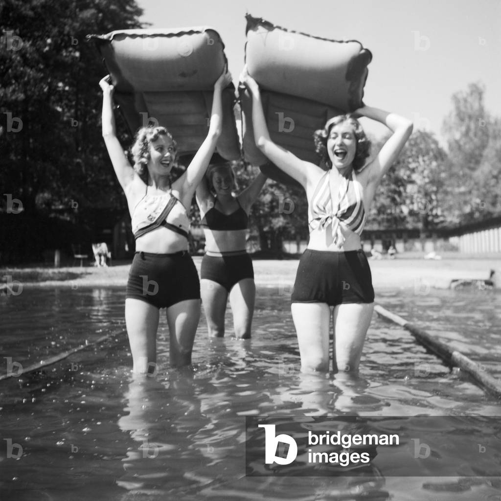 Three young woman taking their air matresses to the water of a lake in the Wachau area in Austria, Germany 1930s (b/w photo)