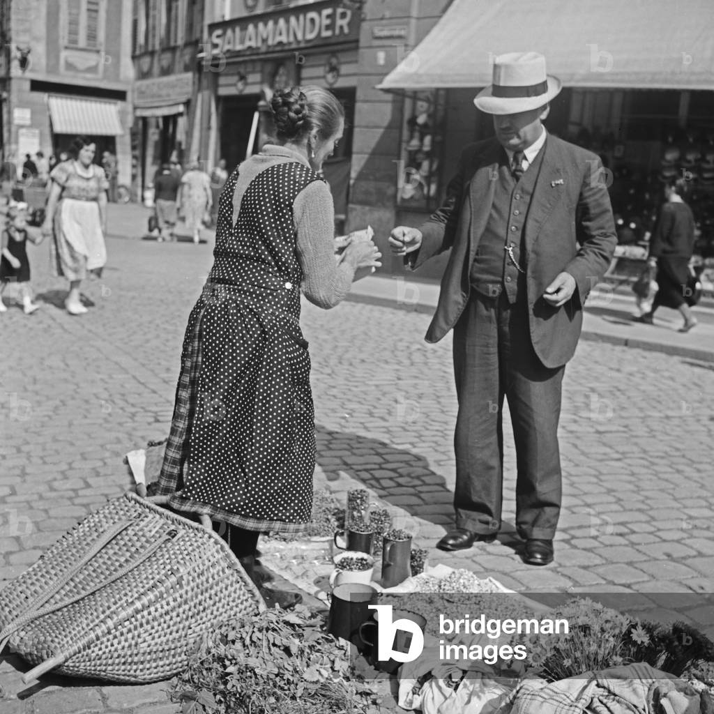 A woman selling flowers on her booth at a market in the city of Regensburg, Germany 1930s (b/w photo)
