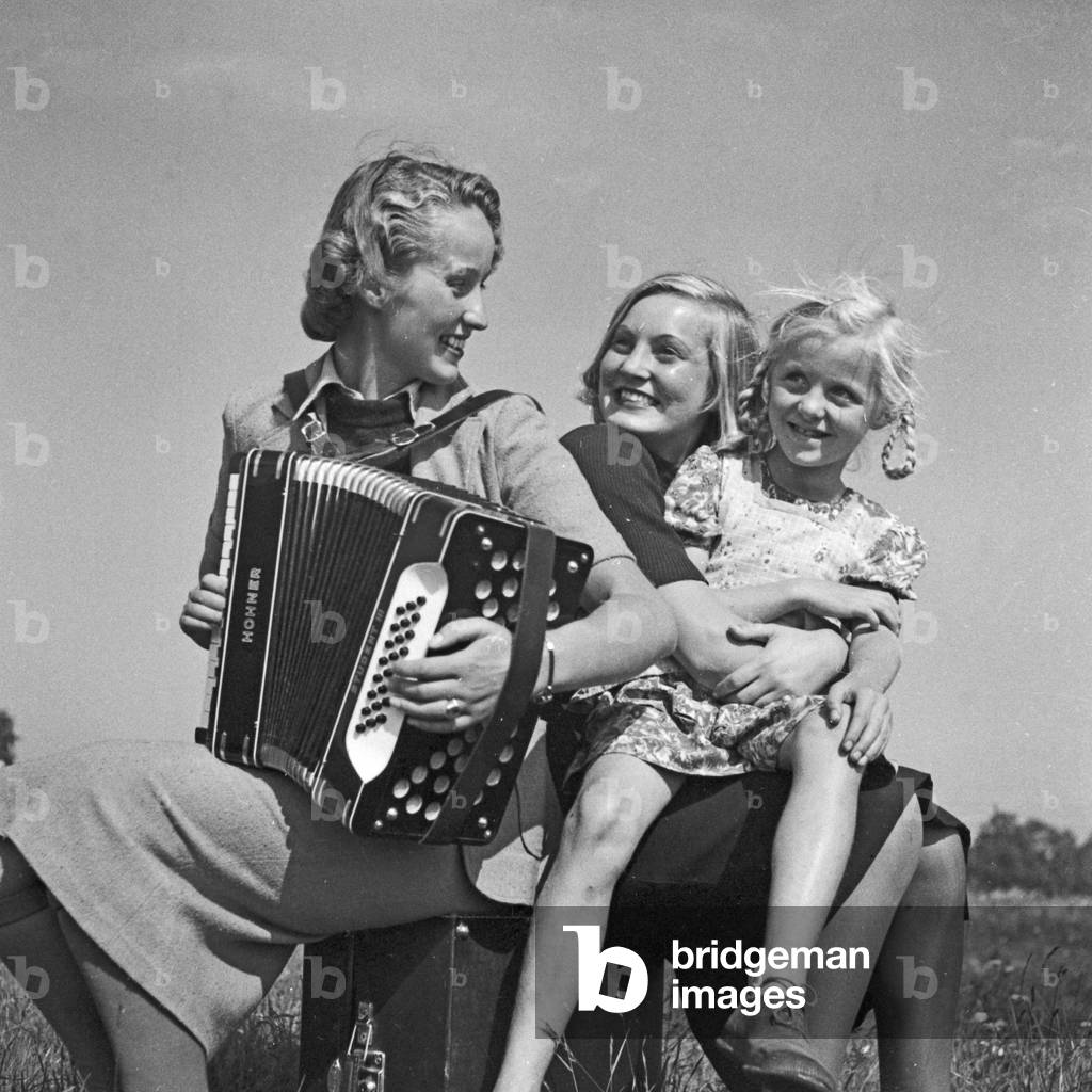 Two women and a little girl playing music with an accordion, Germany 1930s (b/w photo)
