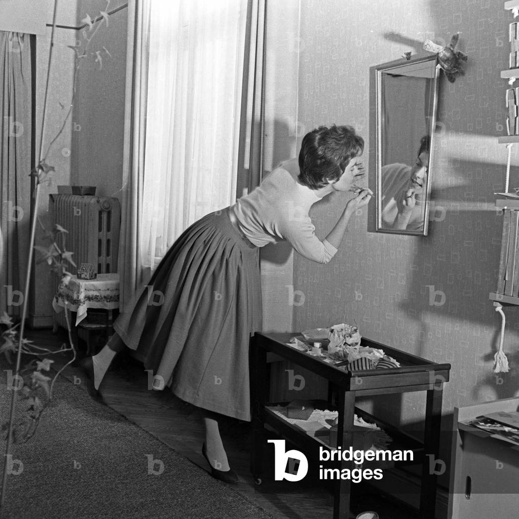 German schlager singer Melitta Berg in a hurry doing the make up in front of a mirror at an entrance hall, Germany 1950s