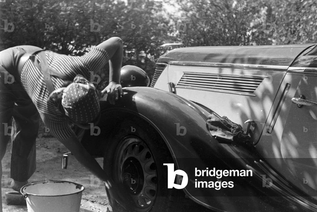 A young woman washing a Ford model Eifel, Germany 1930s (b/w photo)