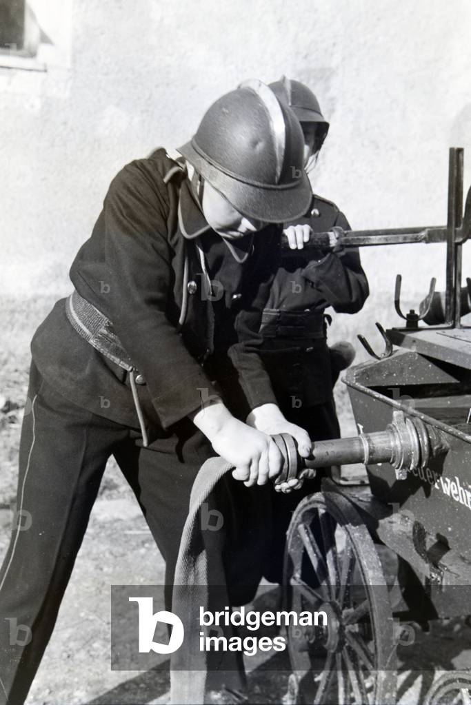 Two uniformed boys of the junior firefighters are installing the water hose during a firefighter training, Germany 1930s (b/w photo)