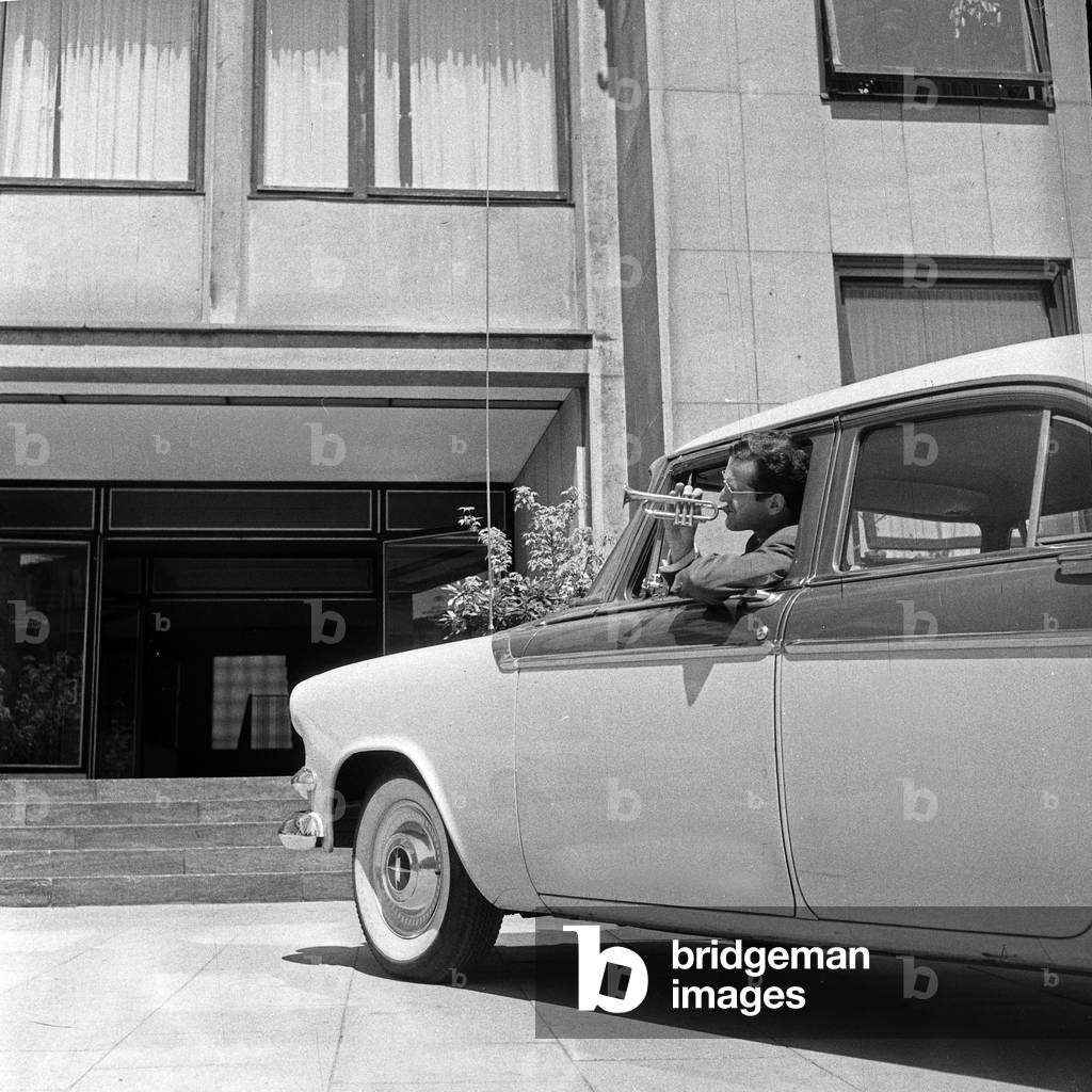 Swiss musician, singer and bandleader Hazy Osterwald driving to the German TV and radio station NDR while playing his trumpet, Germany 1950s