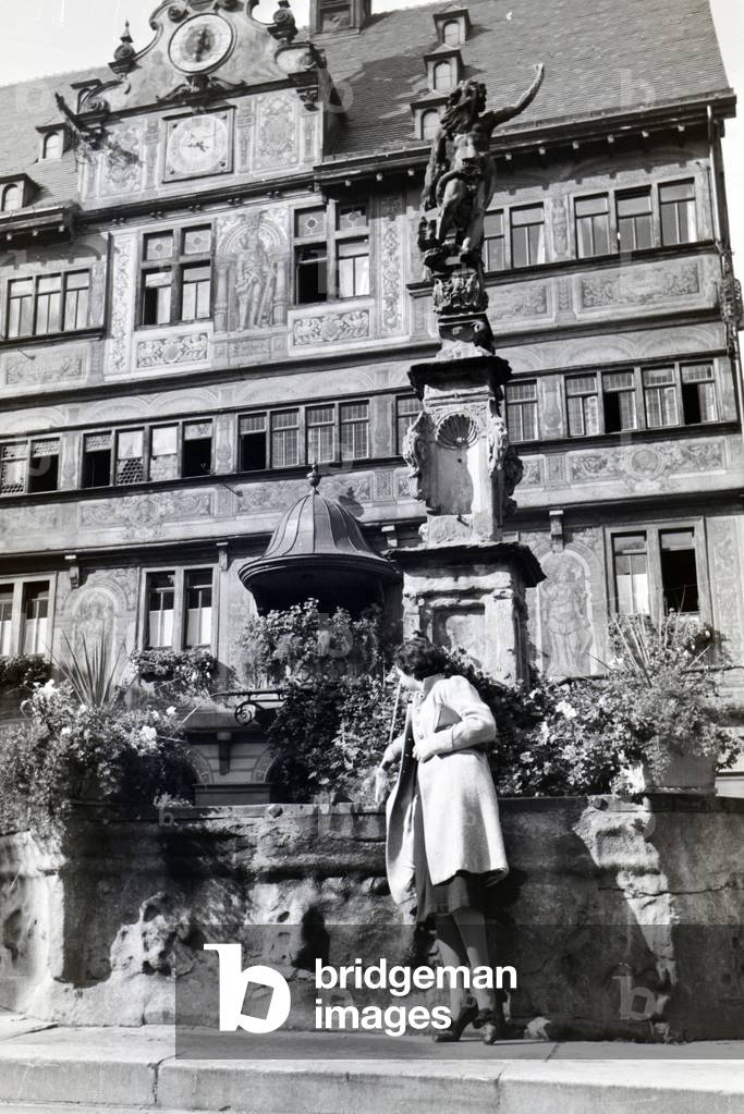A young woman is posing in front of a fountain at the market square in front of the city hall of Tübingen, Germany 1930s (b/w photo)