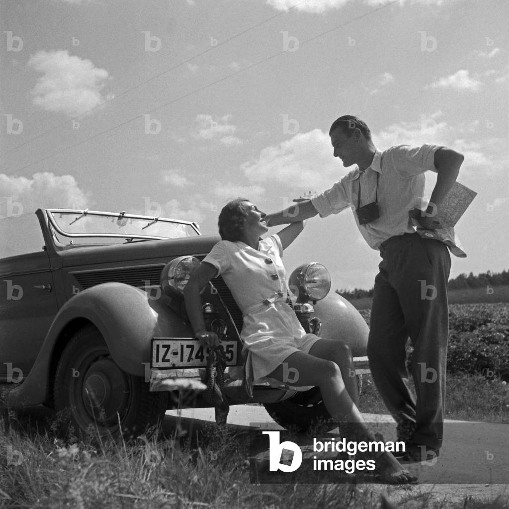 A man and a woman resting in front of their convertible, Germany 1930s (b/w photo)