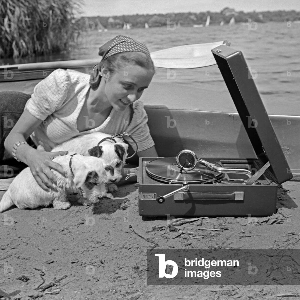Advertising für a Klepper foldboat: a young woman with two puppies lying at the beach listening to a gramophone, Germany 1930s (b/w photo)