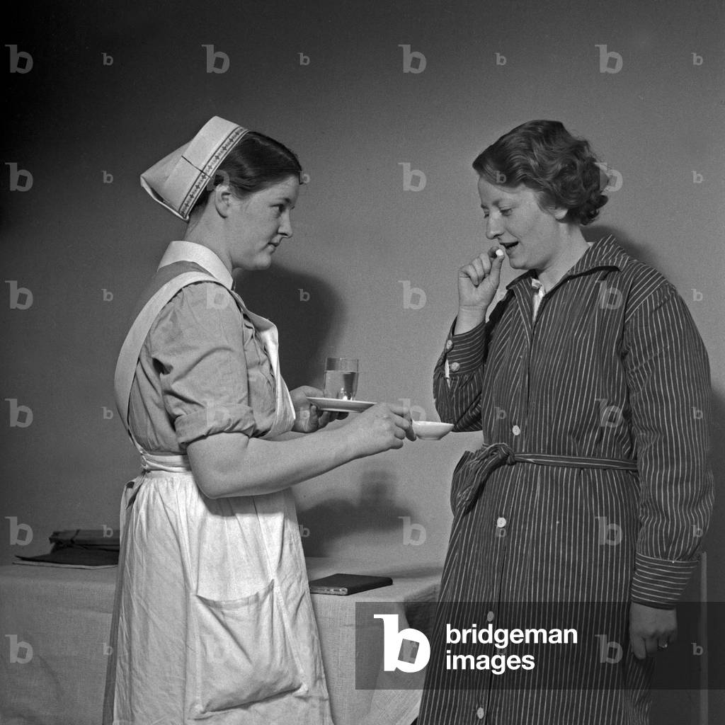 A young nurse of the German Red Cross applying a pill to an ill woman, Germany 1930s (b/w photo)