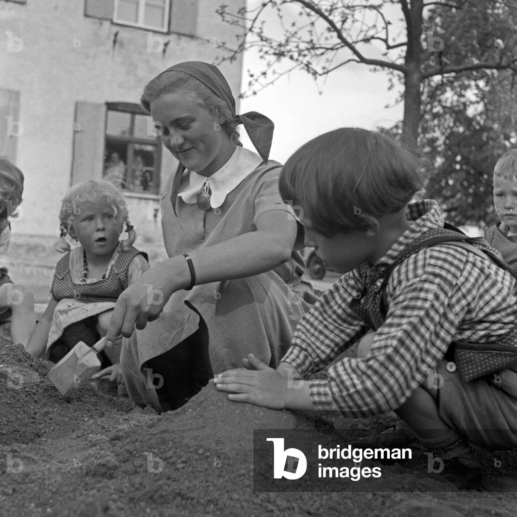 A woman playing with toddlers at the female workforce at Kempten, Germany 1930s (b/w photo)