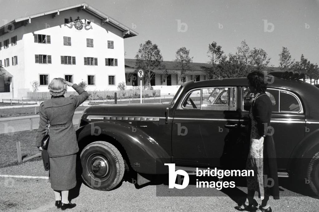 Two young women are looking at the clock on the wall of the city hall at the Chiemsee, Germany 1930s (b/w photo)