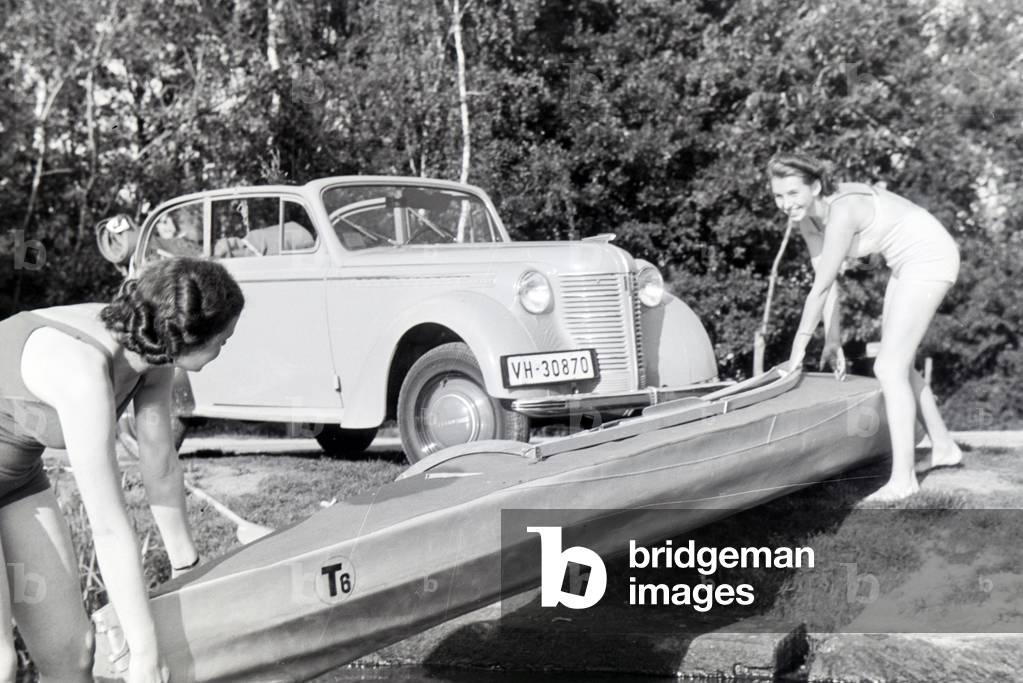 Two young women pulling a boat, Klepper T6 from the coast into the lake, Germany 1930s (b/w photo)