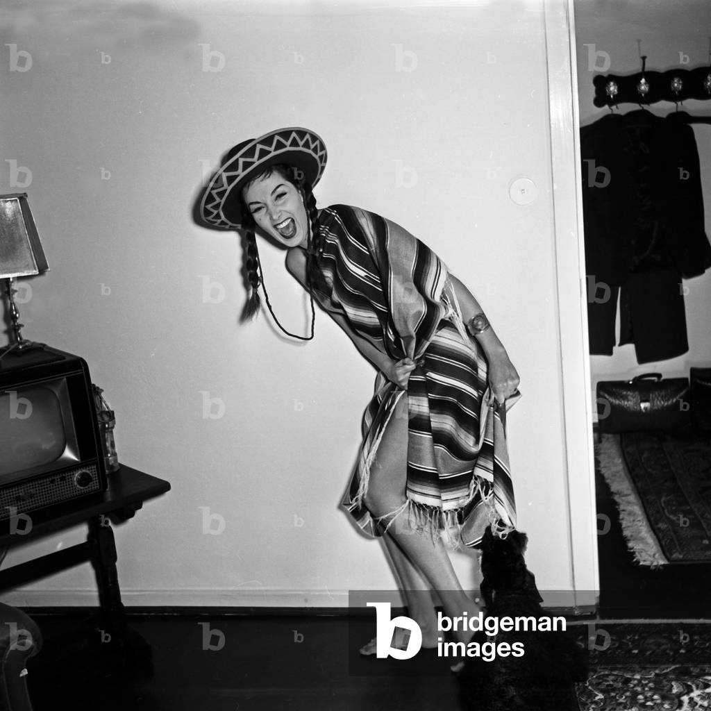 doing a promotional photo shoot wearing a poncho and a sombrero hat with her poodle, Germany 1950s