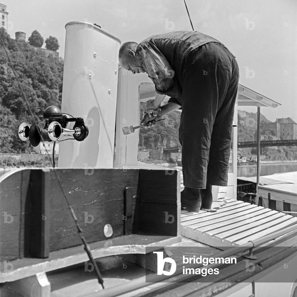 A sailor of one of the steam ships on the Danube has to paint the chimney, Germany 1930s (b/w photo)