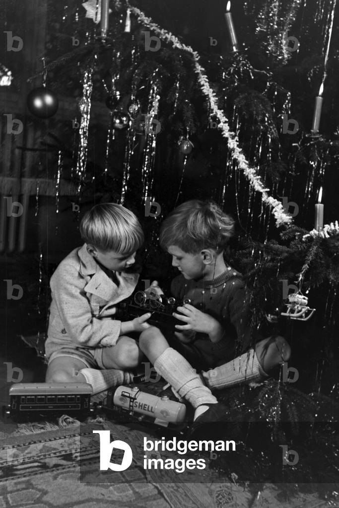 Two boys playing with the new model train under the christmas tree, Germany 1930s (b/w photo)
