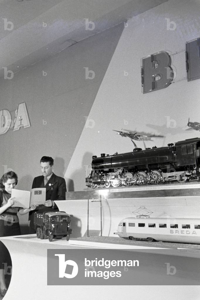 Two Persons in front of a stand with models of the italian mechanical engineering corporation Breda on the Leipziger Frühjahrsmesse, Germany 1941 (b/w photo)