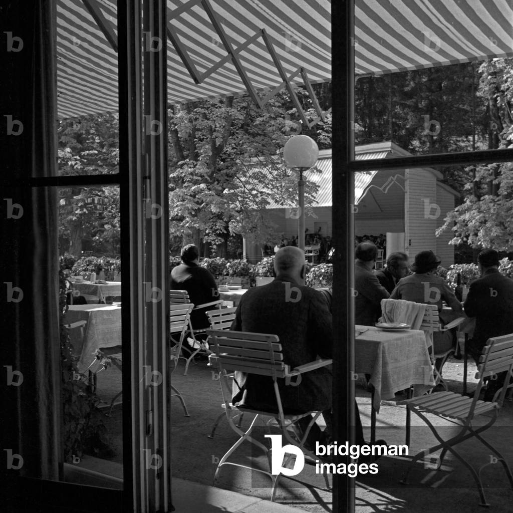 Guests of a terrace restaurant sitting under a blind and listening to the music of the spa orchestra at Wildbad in Black Forest, Germany 1930s (b/w photo)