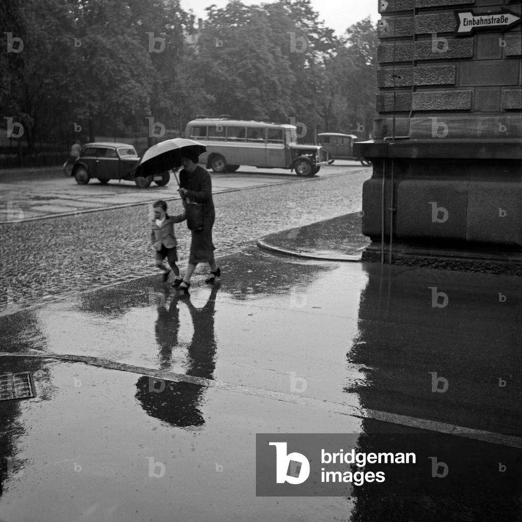 Mother and child in the rain under an umbrella, Germany 1930s (b/w photo)