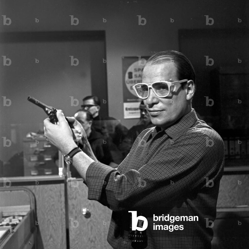 Deutschland 1966, Regisseur Jürgen Roland probiert mit Schutzbrille eine Pistole aus