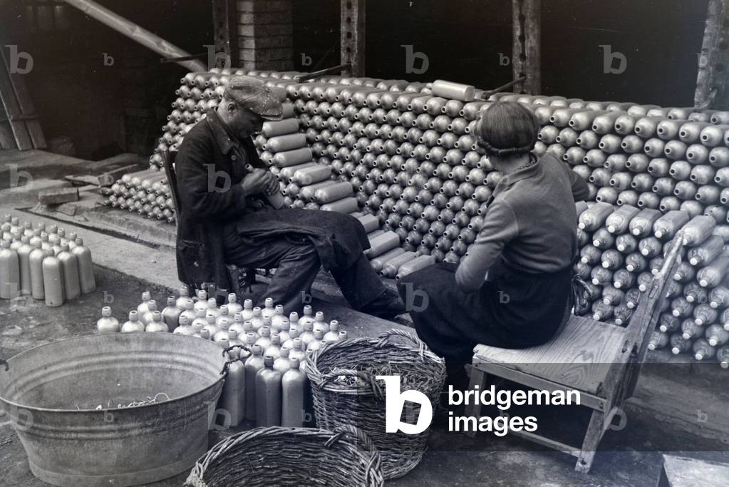 Two master potters from the Kannenbäckerland are fixing the swing tops to the stoneware bottles outdoors, Germany 1930s (b/w photo)