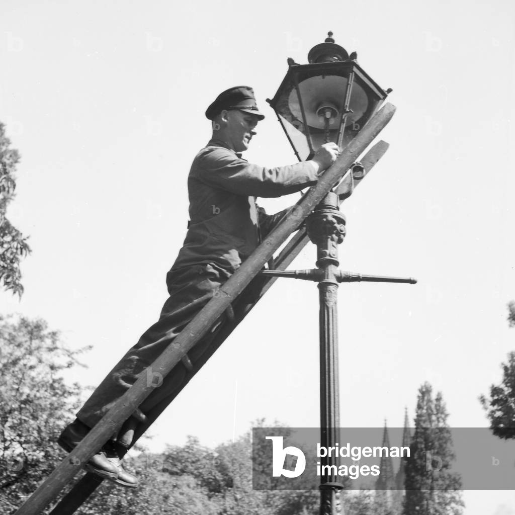 A public servant changing broken bulbs from a street lantern, Germany 1930s (b/w photo)