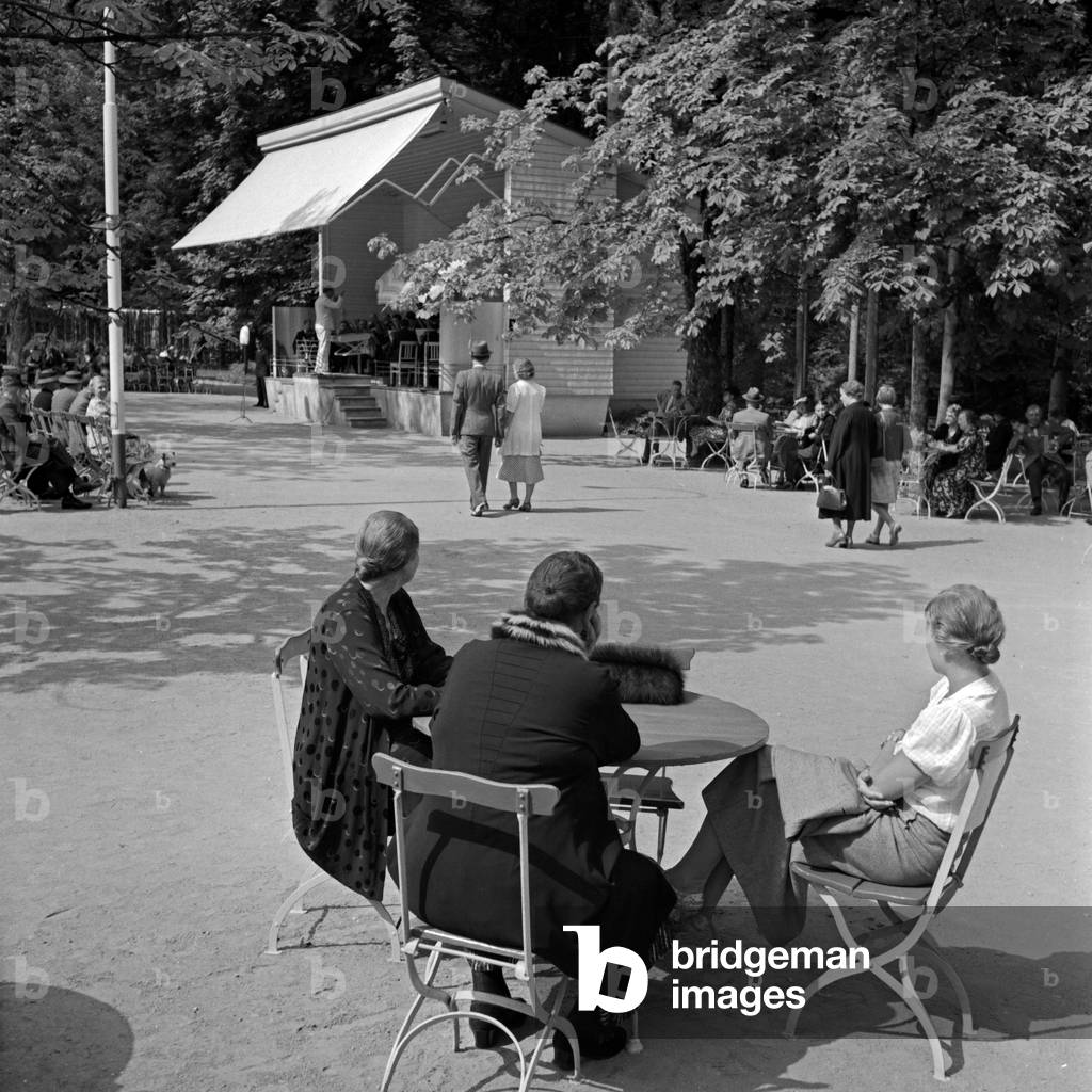 Three women sitting at an outdoor gastronomy and listening to the spa orchestra at Wildbad in Black Forest, Germany 1930s (b/w photo)