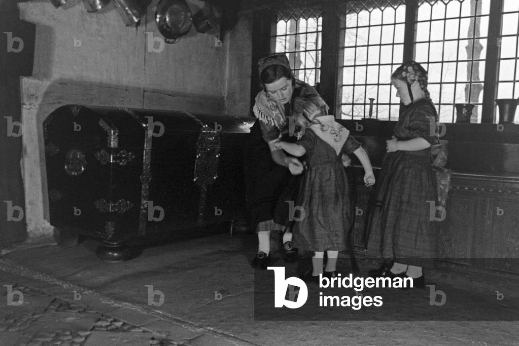A woman helping to little girls to wear traditional costume of Ammerland near Bad Zwischenahn at the Oldenburg area, Germany 1930s (b/w photo)
