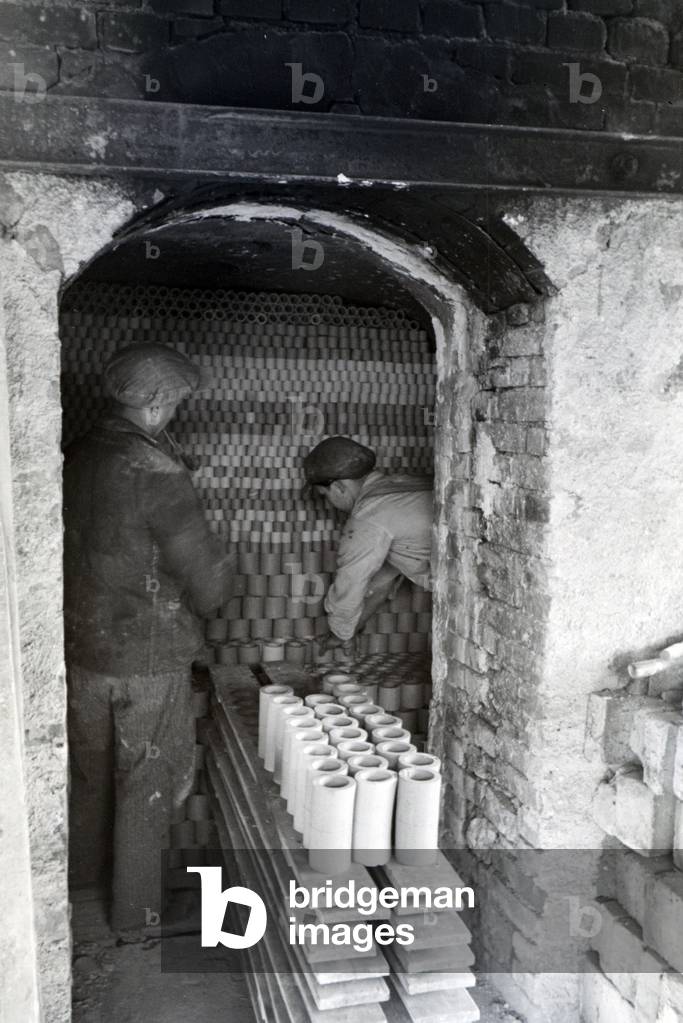 Employees of a stoneware factory are stacking ceramic blanks inside a drying room, Germany 1930s (b/w photo)