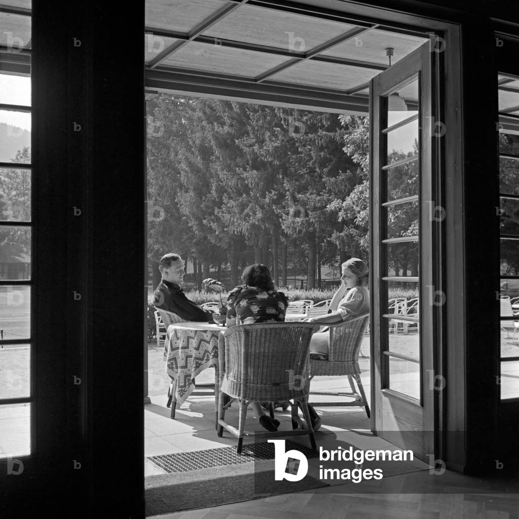 A man and two women sitting in the patio of the spa resort at Herrenalb in Black Forest, Germany 1930s (b/w photo)