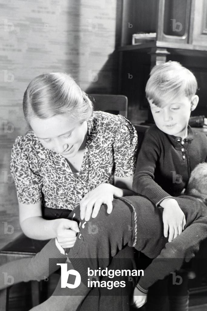 The eldest daughter of a extended family repairing the trousers of her little brother, Germany 1930s