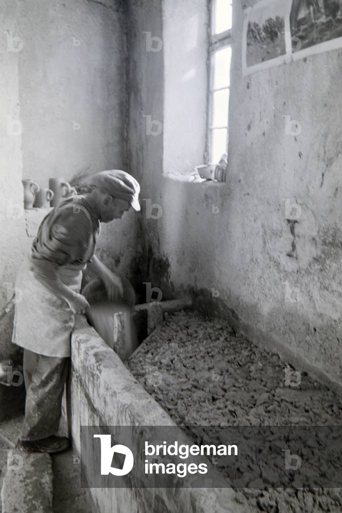 An employee of a stoneware factory in the Kannenbäckerland pouring fresh raw clay inside a basin, Germany 1930s (b/w photo)
