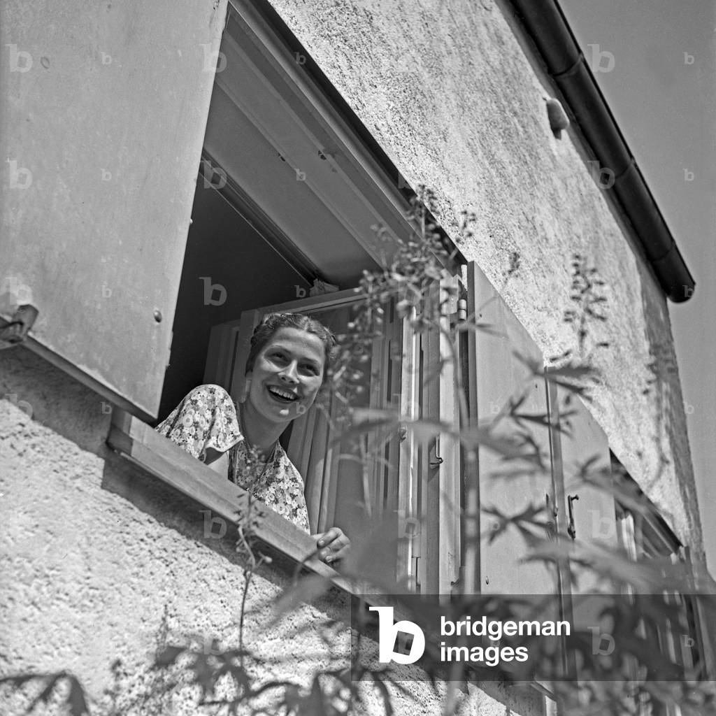 A young woman looking out of the window to her garden, Germany 1930s (b/w photo)