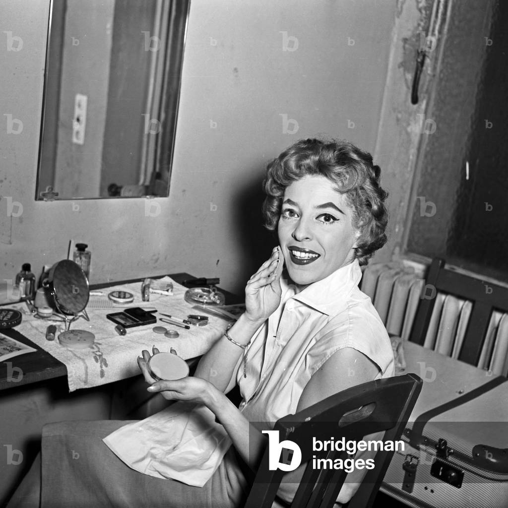 Singer doing her make up in front of the mirror in her wardrobe at Hamburg, Germany 1950s