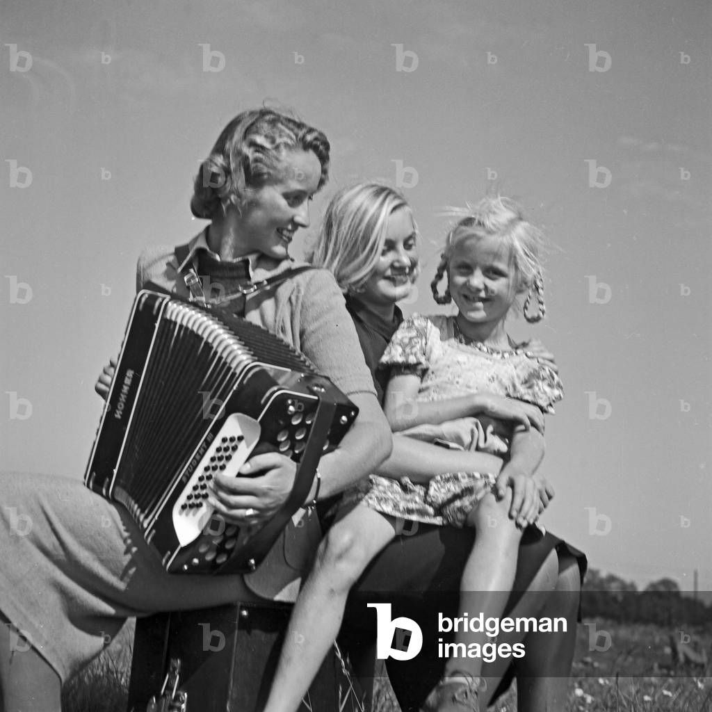 Two women and a little girl playing music with an accordion, Germany 1930s (b/w photo)