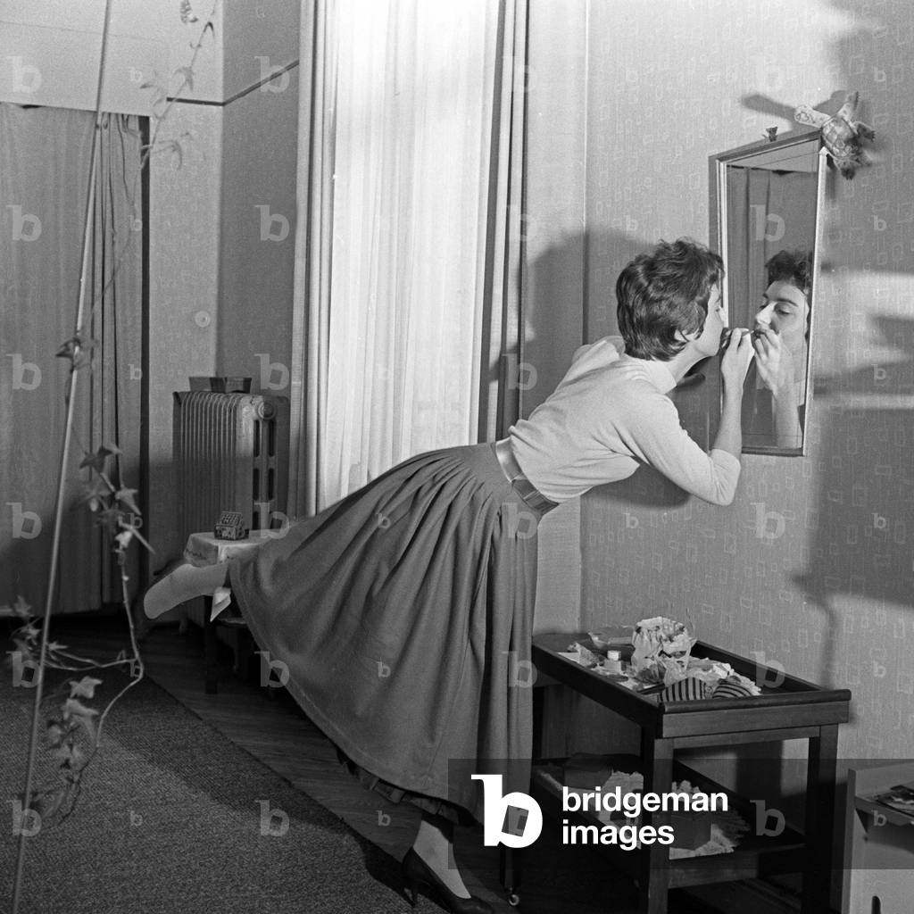 German schlager singer Melitta Berg in a hurry doing the make up in front of a mirror at an entrance hall, Germany 1950s